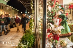 Holiday Stroll in Downtown Mystic photo showing people window shopping and retail windows decorated for Christmas.