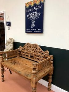 Antique ornate wooden bench in front of a sign for the Indigo Elephant store at the Velvet Mill.