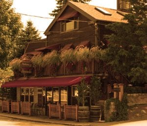Photo of Anthony J's Bistro. A brown wooden building with red awnings and decorated with live plants.