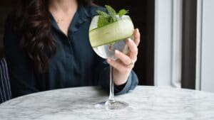 Woman holding gin and tonic with a cucumber and mint leaves in downtown Mystic