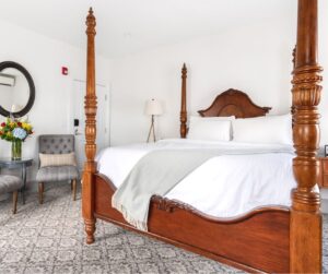 Large king bed in hotel room with chairs and flowers on table in Stonington, CT